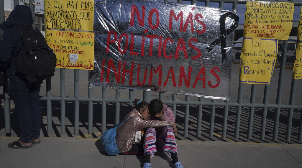 Dos hermanas venezolanas se consuelan sentadas en una vereda ante un centro de detención de migrantes donde docenas de migrantes que temían ser deportado prendieron fuego a las colchonetas, lo que provocó un incendio que mató a docenas de personas, en Ciudad Juárez, México, el martes 28 de marzo de 2023. El cartel dice "No más políticas inhumanas". (AP Foto/Fernando Llano)