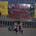 Dos hermanas venezolanas se consuelan sentadas en una vereda ante un centro de detención de migrantes donde docenas de migrantes que temían ser deportado prendieron fuego a las colchonetas, lo que provocó un incendio que mató a docenas de personas, en Ciudad Juárez, México, el martes 28 de marzo de 2023. El cartel dice "No más políticas inhumanas". (AP Foto/Fernando Llano)