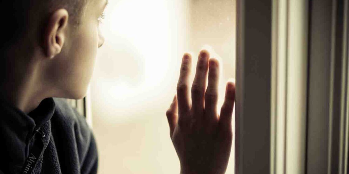 Close up Lonely Orphan Boy in an Orphanage Looking Outside While Holding the Glass Window.