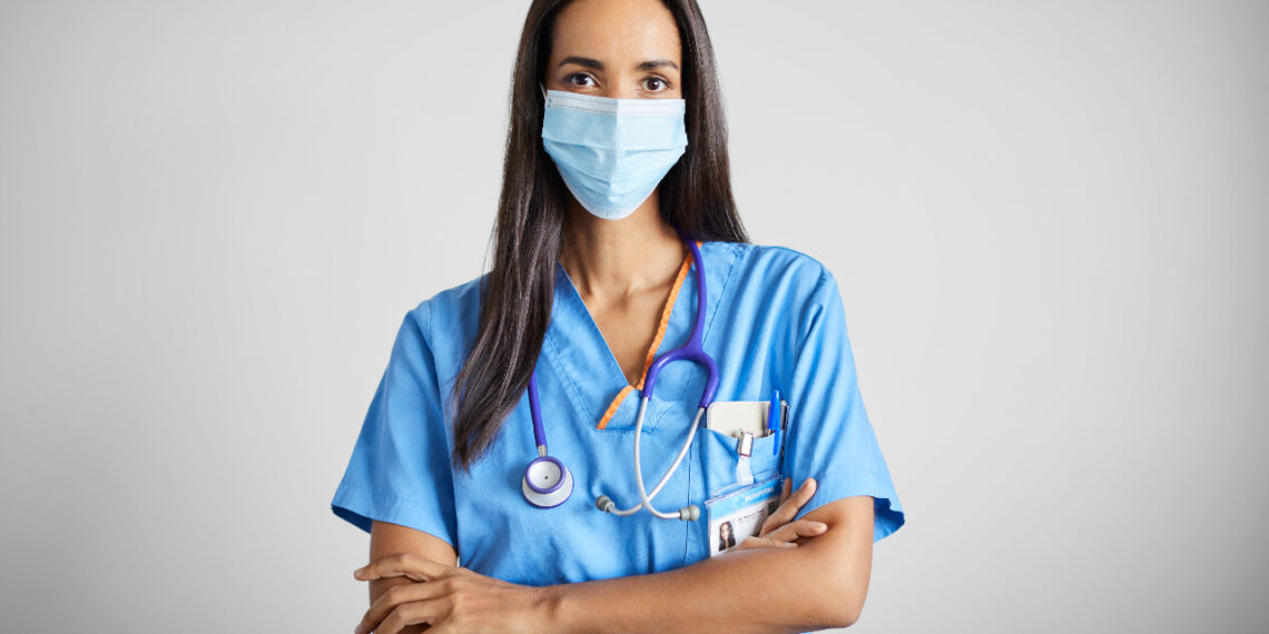 Portrait of Latin American nurse wearing protective face mask. Female healthcare worker is with stethoscope during COVID-19. She is against gray background.